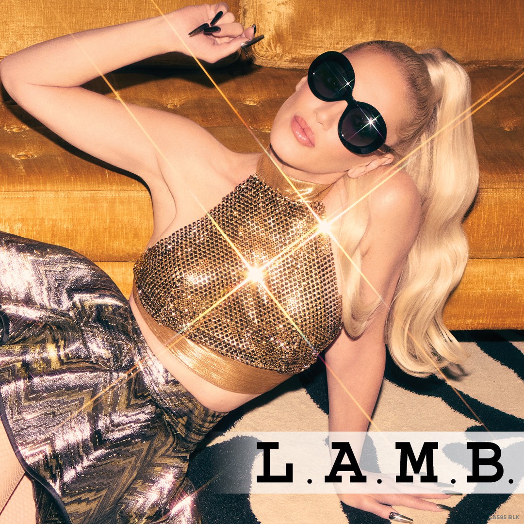 L.A.M.B. LA595 BLK oversized oval black sunglasses with gold detailing and UV400 protection worn by woman in stylish outfit